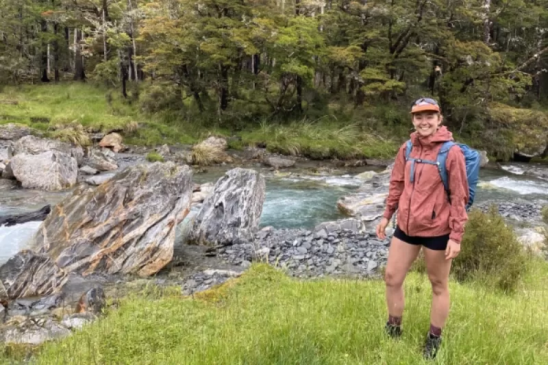 Woman dressed in hiking gear standing on the bank of a rushing river with jagged rocks.
