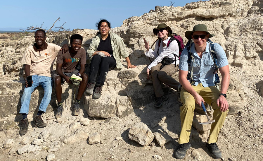 Group of 5 people sitting on a rocky outcrop, smiling at the camera