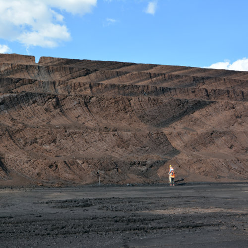 Two people wearing hi-vis standing at the bottom of a huge excavation of black and brown layered soils