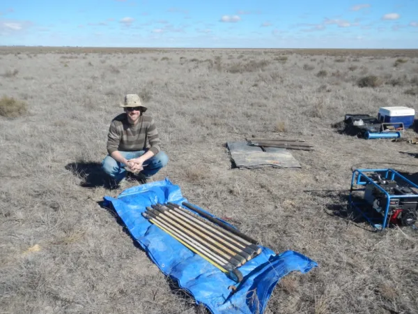 Man squats down with many soil core samplers laying on a tarp in front of him.