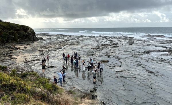 Group of people standing on rock shelf at the beach.