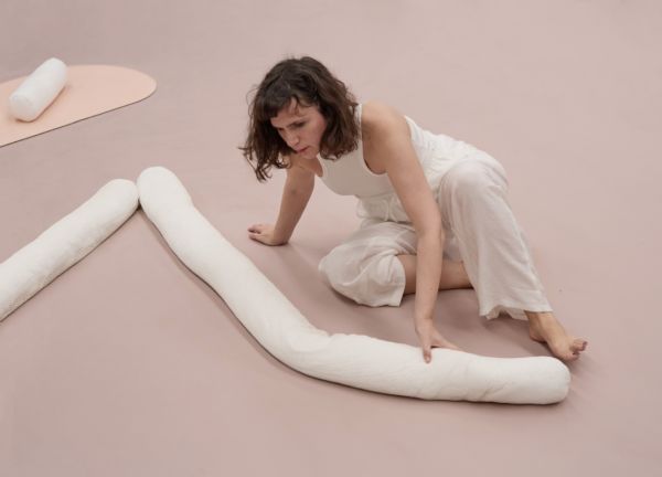 Photograph of performance, woman in white on pink floor moves textile plushy around floor.