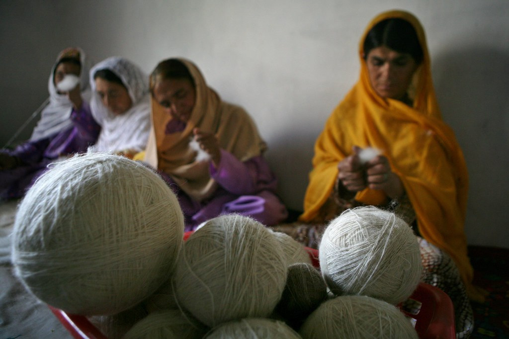 Three women in orange head scarves knitting, sat behind three balls of wool.
