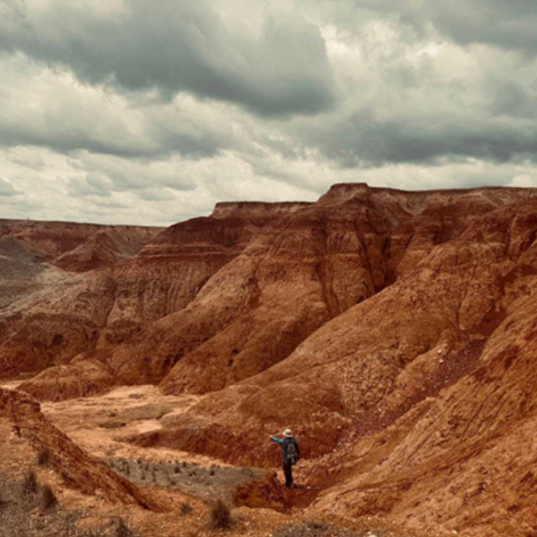 A person walking through a red rocky valley surrounded by mountains.