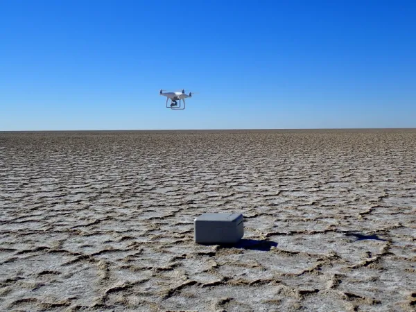 Dried lakebed with drone in sky and equipment case on ground.