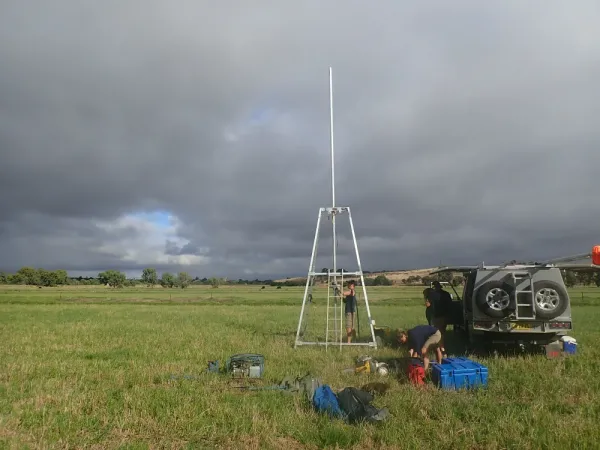 Field site in grassy field, equipment spread out, tripod standing tall above trench.