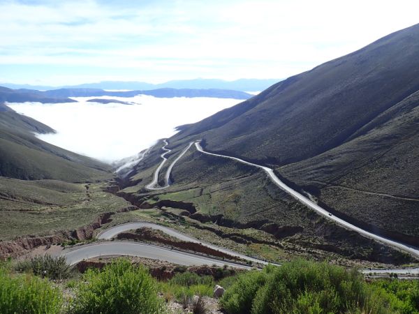 A road full of hairpin turns theading across green mountains decending to the ocean.